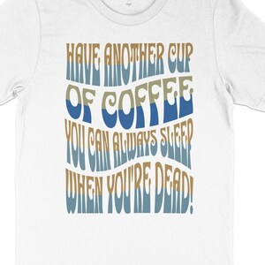 May include: White t-shirt with a blue and brown graphic that says "Have another cup of coffee you can always sleep when you're dead!"