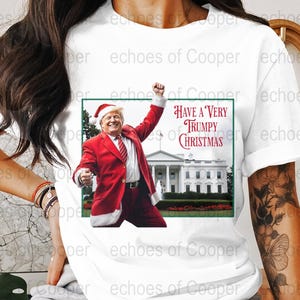 Könnte beinhalten: Weißes T-Shirt mit einem festlichen Aufdruck. Das Design zeigt einen Mann im Weihnachtsmannkostüm, das Weiße Haus und den Text "Have a Very Trumpy Christmas".