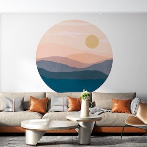 Puede incluir: Un interior de sala de estar con un sofá seccional beige, dos mesas de café y una silla de cuero marrón. La pared detrás del sofá presenta una gran calcomanía de pared circular con un diseño de paisaje de puesta de sol en tonos de rosa, azul y amarillo.