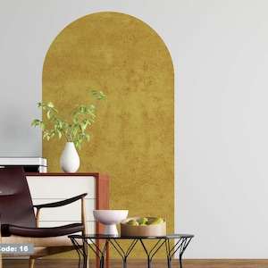 May include: A gold arch wall decal with a textured finish. The decal is applied to a white wall in a living room setting with a brown leather chair, a wooden table, and a vase of green plants.