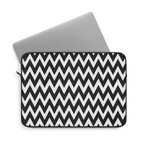 Puede incluir: Una funda para portátil con un patrón de chevrón en blanco y negro con un portátil plateado parcialmente insertado. La funda tiene un cierre de cremallera y un borde negro. El portátil es plateado.