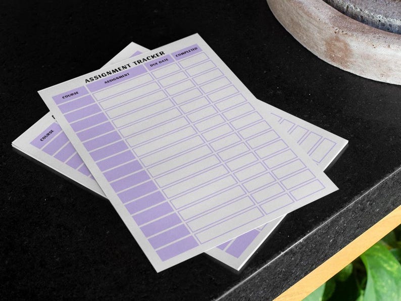 K&ouml;nnte beinhalten: Zwei wei&szlig;e Aufgabenverfolgungsbl&auml;tter mit einem lila Design. Die Bl&auml;tter tragen oben die Worte "Assignment Tracker" mit Spalten f&uuml;r "Kurs", "Aufgabe", "F&auml;lligkeitsdatum" und "Abgeschlossen". Die Bl&auml;tter sind auf einer schwarzen Oberfl&auml;che gestapelt.