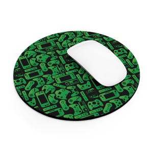 May include: Round black mousepad with a green pattern of video game controllers and consoles. A white computer mouse rests on the pad. The mousepad is designed for use with a computer.