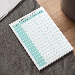 May include: A white assignment tracker notepad with a teal grid design. The notepad is labelled "Assignment Tracker" and includes sections for course, assignment, due date, and completion status. The notepad is on a grey surface.