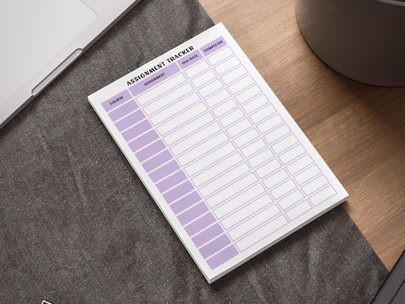 May include: An assignment tracker notepad with a white background and a purple grid design. The notepad is labeled 'Assignment Tracker' at the top. The columns are labeled 'Course', 'Assignment', 'Due Date', and 'Completed'. The notepad is on a dark gray surface.