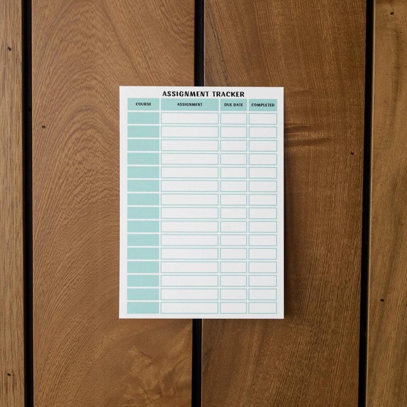以下が含まれることがあります： 上部に「ASSIGNMENT TRACKER」というタイトルが付いた、ターコイズ色のグリッドの白い課題トラッカー。トラッカーは木製の表面にあります。「COURSE」、「ASSIGNMENT」、「DUE DATE」、「COMPLETED」とラベル付けされた列があります。