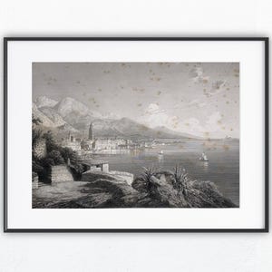 Könnte beinhalten: Schwarz gerahmter Druck einer Vintage-Landschaft. Das Graustufen-Kunstwerk zeigt eine Küstenstadt mit Bergen im Hintergrund, Segelbooten auf dem Wasser und üppiger Vegetation im Vordergrund. Der Druck ist auf weißem Hintergrund montiert.