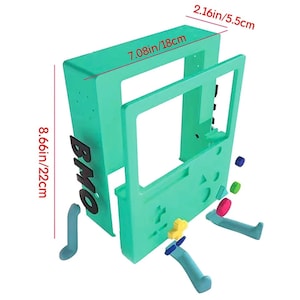 May include: A disassembled teal green plastic game console with the word "BMO" printed on the side. The console is 8.66 inches tall and 7.08 inches wide. The console is made up of several pieces, including the main body, a screen, and two controllers.