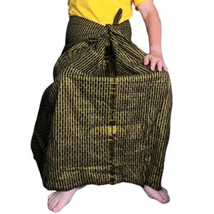 Puede incluir: Un sarong de rayas negras y doradas atado a la cintura. El sarong está hecho de una tela suave y ligera, ideal para usar en climas cálidos.