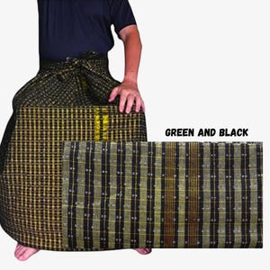 Puede incluir: Un pareo con un patrón de cuadros tejido en tonos verde, negro y dorado. La tela muestra un diseño de cuadrícula con líneas verticales y horizontales. El texto "GREEN AND BLACK" está impreso en el lado derecho de la imagen.