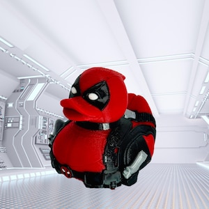 May include: A red and black Deadpool-themed rubber duck. The duck has a red head and body with black accents, including a mask, utility belt, and backpack. The toy is set against a futuristic, white background.