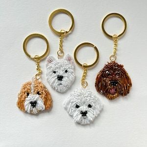 May include: Four beaded dog keychain charms. The charms are white, brown, and tan. The charms are attached to gold key rings.