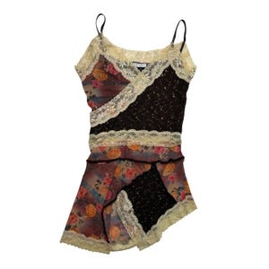 Puede incluir: Una camiseta sin mangas tipo camisola con un diseño de patchwork de tela negra con motas blancas y tela floral transparente en tonos rojos, naranjas y azules. La prenda está decorada con encaje de color crema y tirantes finos.