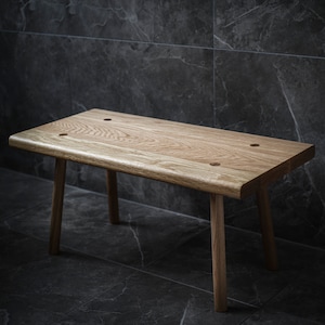 May include: A wooden bench with a natural finish and four legs. The bench is made of solid wood and has a simple, rustic design.