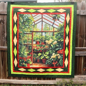 May include: A quilted wall hanging featuring a detailed image of a greenhouse filled with potted plants and flowers. The quilt has a green border with red and yellow diamond accents, creating a vibrant and decorative piece.