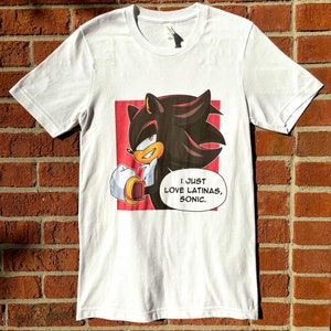 May include: White t-shirt with a red background featuring a cartoon character with black hair and red eyes. The character is holding a golden ring and the text "I JUST LOVE LATINAS, SONIC." is below the character.