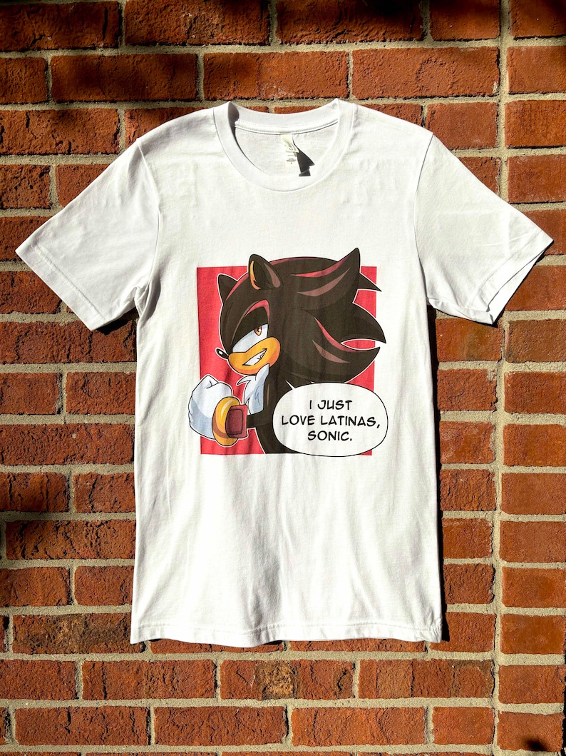May include: White t-shirt with a red background featuring a cartoon character with black hair and red eyes. The character is holding a golden ring and the text "I JUST LOVE LATINAS, SONIC." is below the character.
