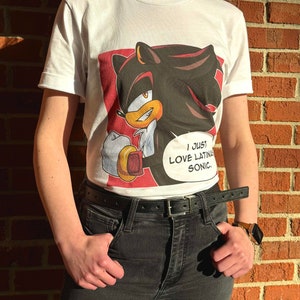 May include: White t-shirt with a graphic print of Shadow the Hedgehog from the Sonic the Hedgehog video game series. The graphic features Shadow with a speech bubble that says "I just love Latina Sonic."