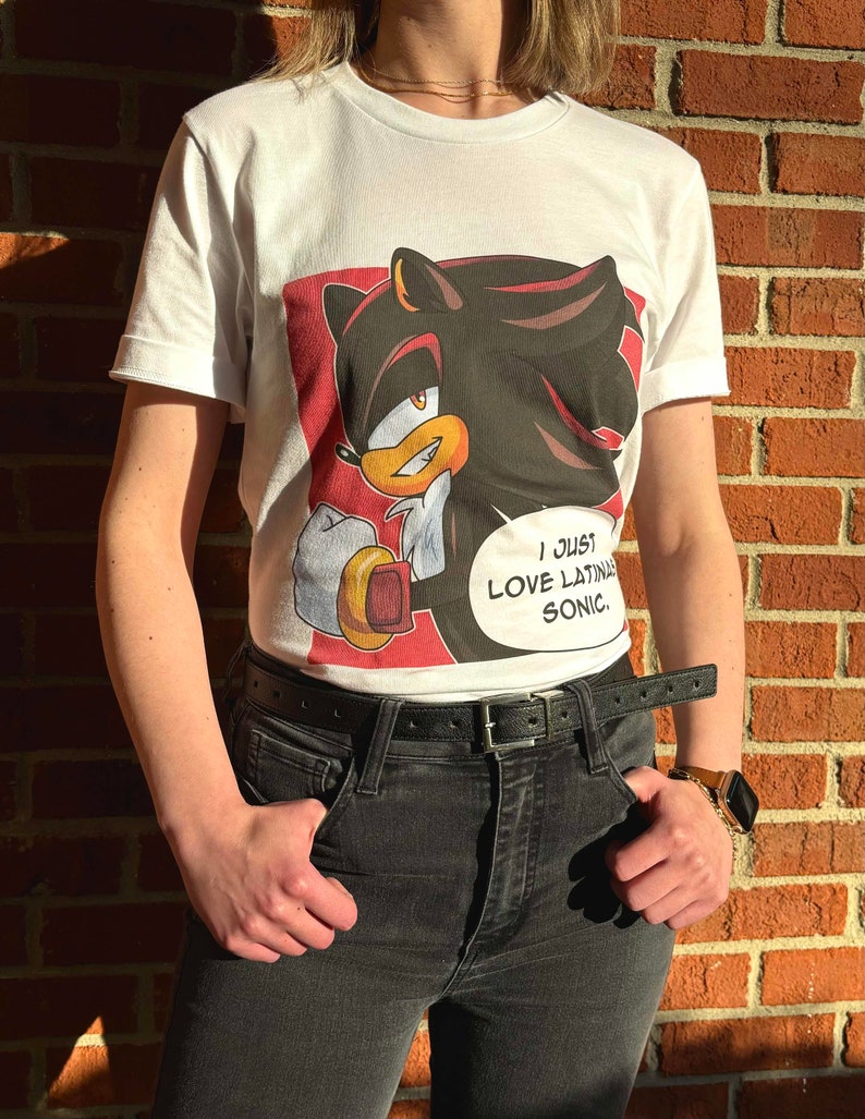 May include: White t-shirt with a graphic print of Shadow the Hedgehog from the Sonic the Hedgehog video game series. The graphic features Shadow with a speech bubble that says "I just love Latina Sonic."