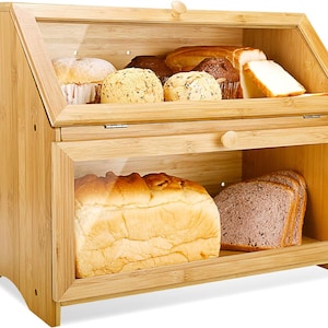 May include: A wooden bread box with a glass lid and a glass door on the bottom. The bread box is filled with various loaves of bread.