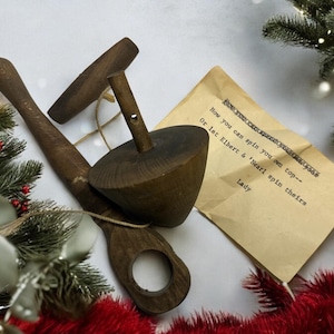 May include: A wooden spinning top and a wooden handle are displayed on a white surface, accompanied by a handwritten note. The top is dark brown, with a conical shape. The note reads, "Now you can spin your own top-- Or let Elbert & 'Nearl spin theirs Lady."