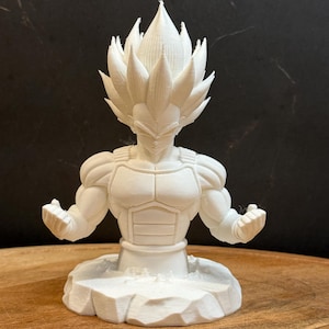 May include: A white 3D-printed figurine of a muscular character with spiky hair and a determined expression. The figure is posed with open hands and is set on a textured base. The figurine is a bust, showing the upper body.