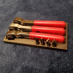 May include: A set of three ratcheting wrenches with red handles and a black holder. The wrenches are silver and black, with the brand name "MAC" visible on the handles. Several screwdriver bits are also included.