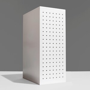May include: A white, rectangular cabinet with a pegboard design on one side. The cabinet is tall and narrow, with evenly spaced holes. The cabinet is set against a gray background and a white surface.