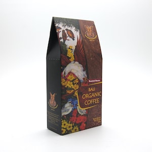 Könnte beinhalten: Eine schwarze und braune Schachtel mit Bali Organic Coffee. Die Schachtel hat ein farbenfrohes Design mit Vögeln, Blumen und dem Text "Bali Organic Coffee". Die Schachtel steht auf einer weißen Oberfläche.