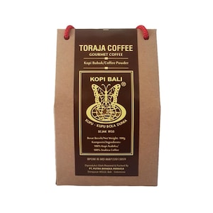 Könnte beinhalten: Eine braune Papiertüte mit einem roten Kordelgriff. Die Tüte hat ein Etikett mit goldener Schrift, auf dem steht "Toraja Coffee Gourmet Coffee Kopi Bubuk/Coffee Powder Kopi Bali KUPU-KUPU BOLA DUNIA SEJAK 1935 Berat Bersih/Net Weight: 100g Komposisi/Ingredients: 100% Kopi Arabika/ 100% Arabica Coffee BPOM RI MD 868722013059 Diproduksi Oleh Roasted & Packed By PT. PUTRA BHINEKA PERKASA Denpasar 80222, Bali Indonesia"