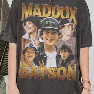 Puede incluir: Una camiseta negra con un estampado gráfico vintage de un joven con el nombre "Maddox Batson" en letras doradas. El gráfico presenta múltiples imágenes del hombre en diferentes poses.