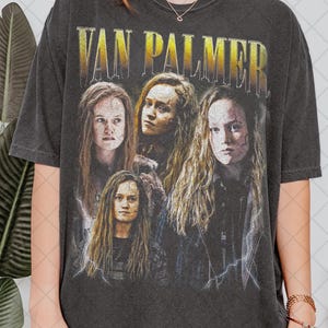Pode incluir: T-shirt cinzenta escura com o texto dourado "VAN PALMER". A camisa apresenta uma colagem de quatro retratos de uma pessoa com cabelo longo e ondulado. O design inclui gráficos de raios.