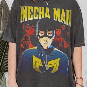 Könnte beinhalten: Dunkelgraues T-Shirt mit dem Text "MECHA MAN" in Gelb. Die Grafik zeigt einen Superhelden in einem blau-gelben Anzug und einer schwarzen Maske. Weitere Figuren sind im Hintergrund, mit einem Vintage-Look.