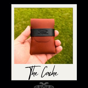 May include: A tan leather card holder featuring a black leather strap across the center. The black strap is embossed with the text HAND CRAFTED BY WITHERED LEATHERWORKS. Below the image, the text reads The Cache, with a moth icon and brand name.