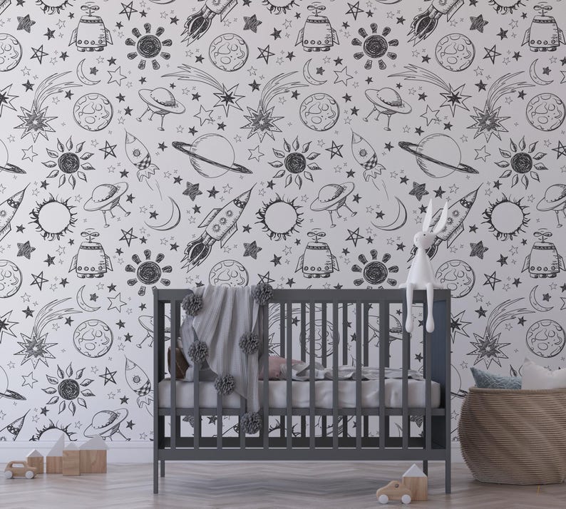 May include: Black and white space-themed wallpaper with a repeating pattern of stars, planets, rockets, and UFOs. The wallpaper is shown in a nursery setting with a crib and a stuffed animal.