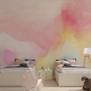 May include: Two twin-sized beds with white bedding and colourful pillows in a room with a watercolour wall mural. The mural features shades of pink, yellow, and blue.