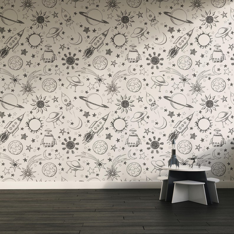 May include: A white wall with a black and white space-themed pattern. The pattern includes stars, planets, rockets, and UFOs. A white table with a black top sits in front of the wall.