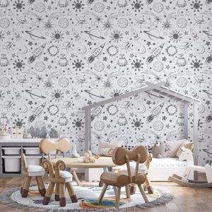 May include: A white wall with a black and white space-themed wallpaper featuring rockets, planets, stars, and moons. The wallpaper is in a child's room with a white crib, a rocking horse, and a table with chairs.