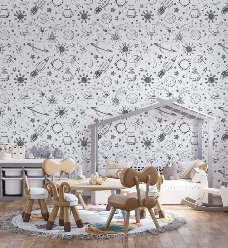 May include: A white wall with a black and white space-themed wallpaper featuring rockets, planets, stars, and moons. The wallpaper is in a child's room with a white crib, a rocking horse, and a table with chairs.