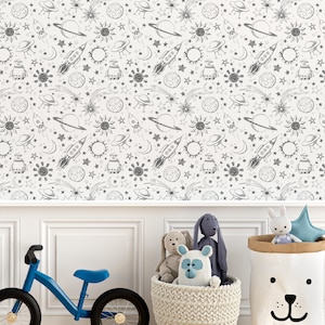 May include: A white wall with a black and white space-themed wallpaper featuring rockets, planets, stars, and suns. A blue children's bicycle is in the foreground, and a basket of stuffed animals is in the lower right corner.