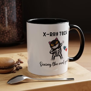 May include: White ceramic mug with a black rim and handle. The mug features a black cat with a skeleton costume and the text "X-Ray Tech Seeing the real you".