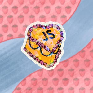 May include: A heart-shaped cake sticker with a holographic finish. The cake is yellow with pink frosting and the letters "JS" in black on the front.