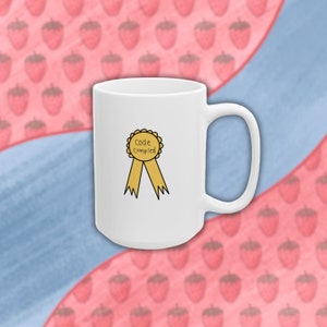May include: White ceramic coffee mug with a yellow ribbon and a gold circle with the text "Code Compiled" on it.