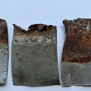 May include: Three irregularly shaped metal pieces with a rusted, textured surface. The top edges are jagged and heavily corroded with shades of brown and orange, while the lower portions are a dull gray.