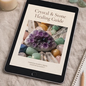 Puede incluir: Una tableta digital muestra el título "Crystal & Stone Healing Guide" sobre una foto de varios cristales. Una geoda de amatista es el punto focal, rodeada de otras piedras coloridas. Una vela encendida y un bloc de notas con un lápiz están en el fondo.