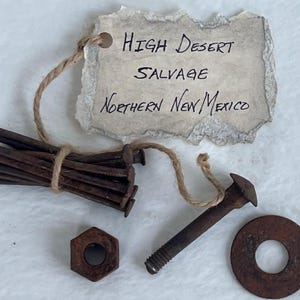 May include: A collection of rusty metal hardware, including nails, a bolt, a washer, and a nut, tied together with twine. A tag with the text "High Desert Salvage Northern New Mexico" is attached.
