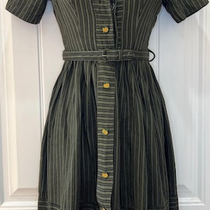 May include: A green and black striped dress with short sleeves and a button-up front. The dress has a belt and pumpkin-shaped buttons.
