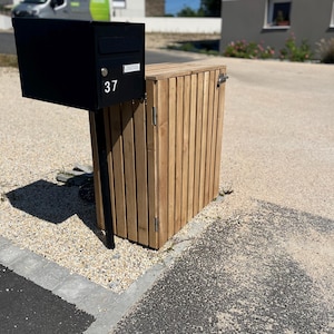 Könnte beinhalten: Ein schwarzer Metallbriefkasten mit der Nummer 37 ist auf einem Holzschrank montiert. Der Schrank besteht aus vertikalen Holzlatten. Der Briefkasten befindet sich auf einem schwarzen Metallpfosten. Der Schrank hat eine Scharniertür.