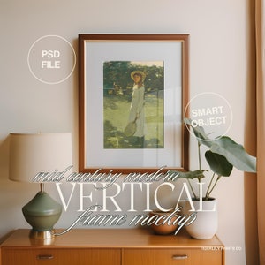 May include: A brown wood frame with a white mount and a painting of a girl in a white dress holding a tennis racket. The frame is on a wooden dresser with a lamp and a plant. The text "mid century modern VERTICAL frame mockup" is written in white on the dresser.