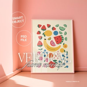 May include: A vertical framed art print featuring a colorful illustration of various fruits, including strawberries, lemons, watermelon, and a banana. The frame is a soft pink color, and the text "VERTICAL frame mockup" is displayed on the artwork.